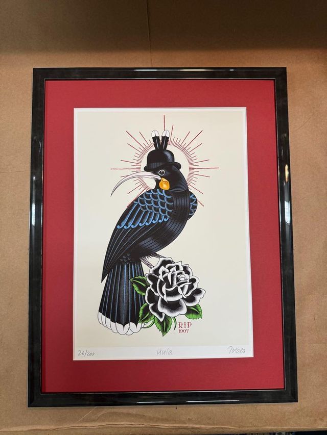 A print of a black bird with a rose in a glossy black frame with a red mat