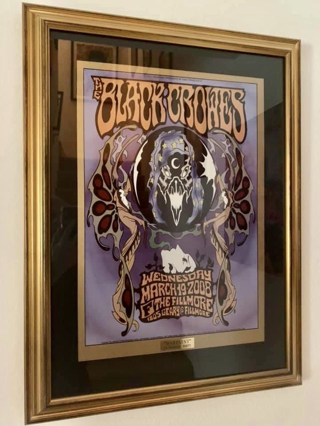 A Black Crowes concert poster in a gold frame with a black mat and a small engraved nameplate