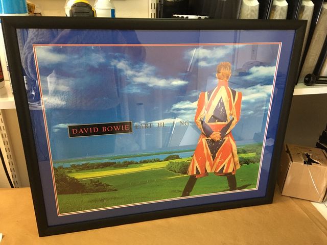 A David Bowie poster in a black frame with a blue mat and a thin red accent line