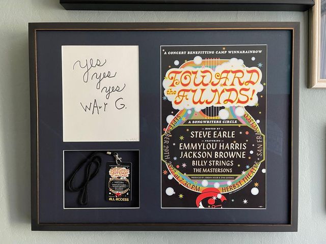 A concert poster, a handwritten note and a backstage lanyard, each in its own opening of a dark mat, in a silver frame