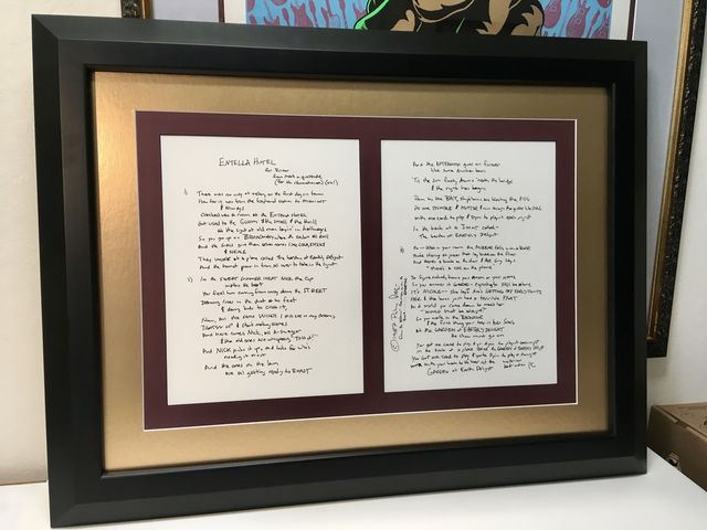 Two handwritten pages side by side in a black frame with burgundy and gold mats
