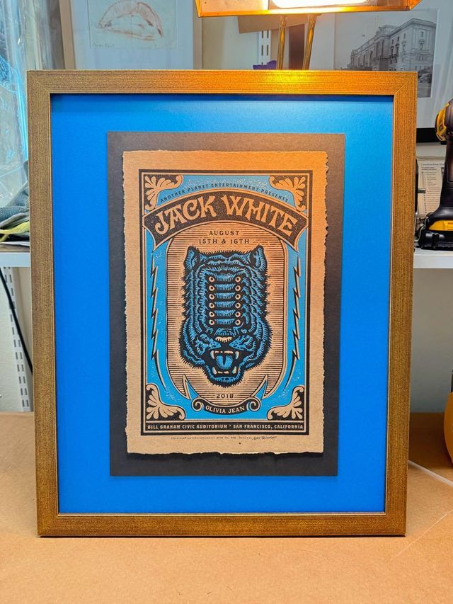 A Jack White poster with a tiger illustration, floated on a dark panel over a bright blue mat in a warm wood frame