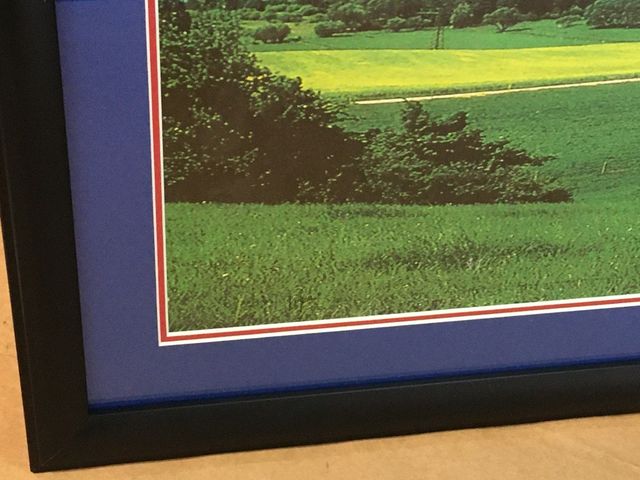 Close-up of a frame corner: a black moulding, a royal blue mat and a thin red accent line around a landscape print