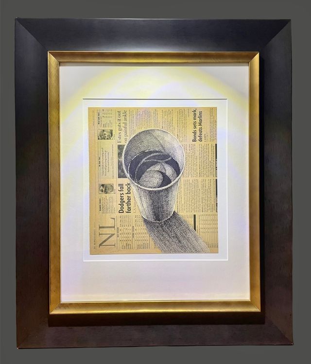 A drawing on newspaper pages in a gold frame set inside a wide dark frame