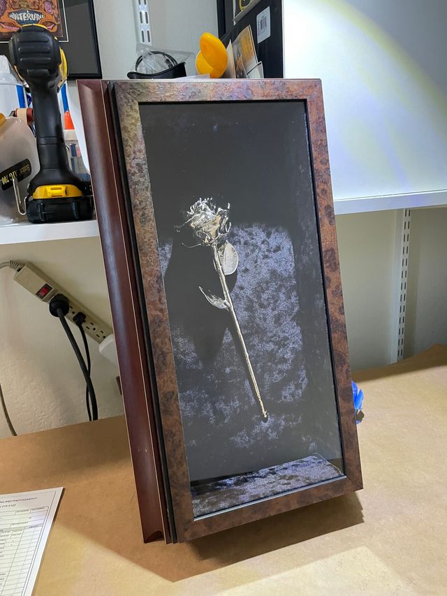 A single rose mounted on a dark textured backing inside a deep burl wood shadow box