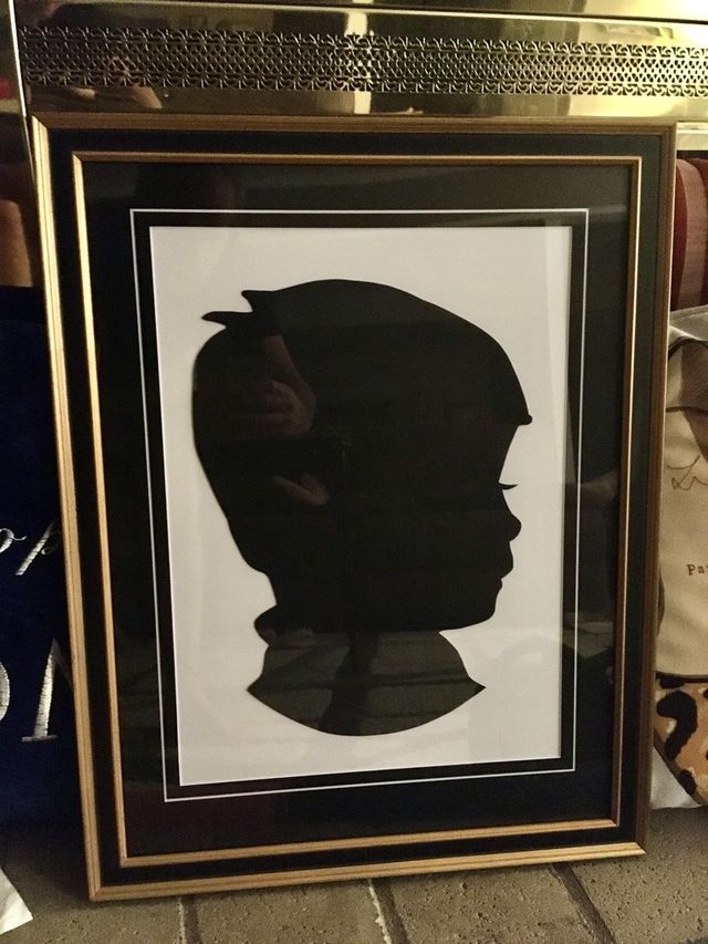 A black paper silhouette portrait of a child in a gold frame with a black mat