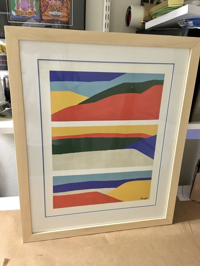 A colorful abstract print of wavy stripes in a natural wood frame with a white mat