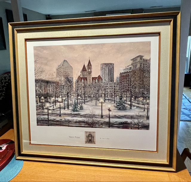 A print of a snowy city park scene in a gold frame with layered mats