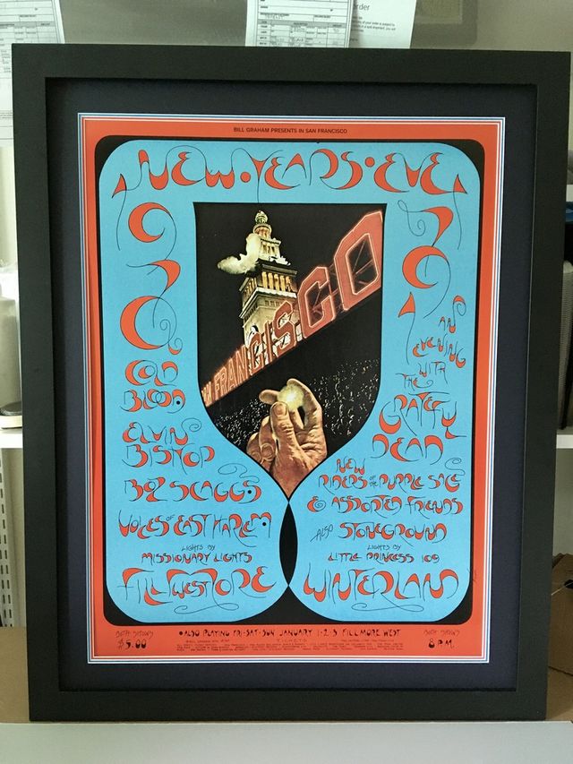 A psychedelic concert poster with ornate blue and orange lettering in a black frame